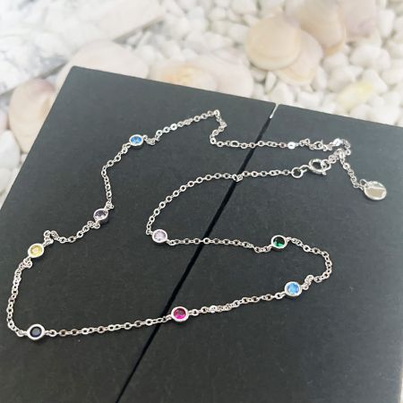 Gros plan sur la délicate chaîne en argent et le charm en pierre CZ multicolore vibrant.