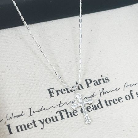 The sterling silver cross necklace displayed on a stylish fabric background for a product advertisement.