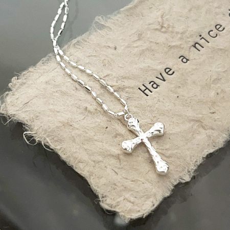 Detailed shot of the silver cross necklace with a textured surface, resting on a beige fabric.