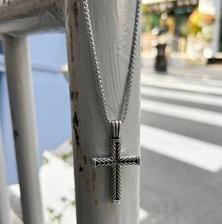 A stylish silver cross pendant necklace for men, shown in an urban setting.