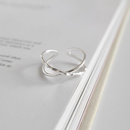 Close-up of the sterling silver crossover ring on a book, highlighting its polished finish and open ring style.