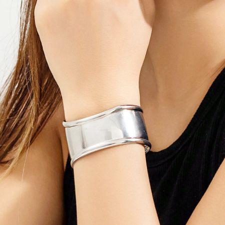Un singolo bracciale a manica punk in argento indossato sul polso di una donna per un look minimalista.