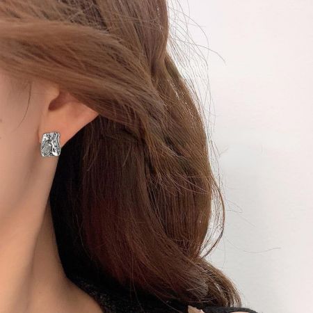 銀メッキの不規則な形のスタッドピアスを着用した女性のクローズアップ。