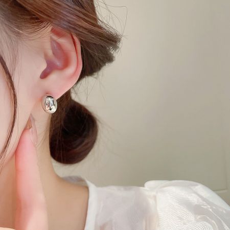 Primo piano di una donna che indossa orecchini a perno a forma di fagiolo piccolo in argento sterling 925.