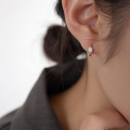 Close-up of a single 925 silver huggie hoop earring with a white oval gemstone.