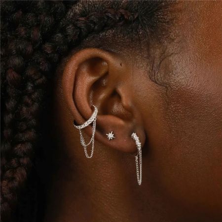 Una collezione di orecchini in argento, incluso l'orecchino a clip con nappina a catena, sull'orecchio di un modello.