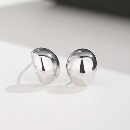 Un paio di orecchini a perno a forma di fagiolo piccolo in argento sterling 925 lucido su una superficie neutra.