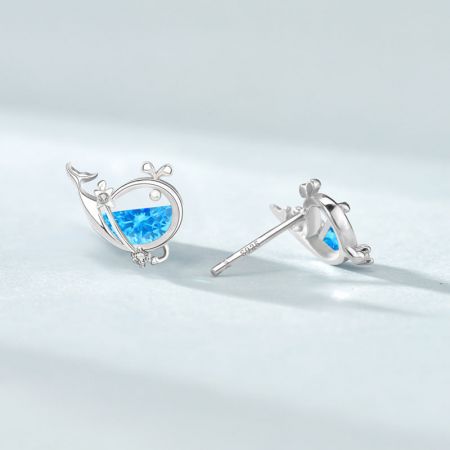 Primo piano di un paio di orecchini huggie in argento del set, con intricati disegni di foglie e fiori con gemme blu.