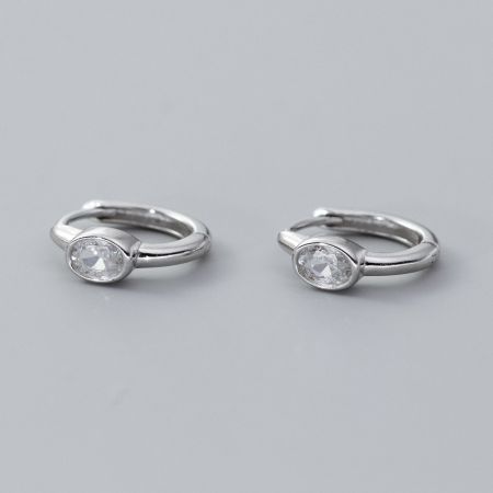 A pair of sterling silver huggie hoop earrings featuring clear, sparkling oval gemstones.