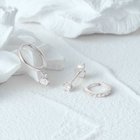 Scatto ravvicinato del prodotto di tre paia di orecchini in zirconia argentata su uno sfondo bianco testurizzato.
