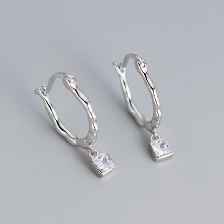 Vue détaillée des boucles d'oreilles en argent torsadées avec des pierres en zircon carrées et transparentes.