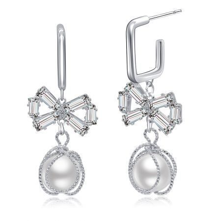 Toma detallada de los pendientes de lazo plateados que destaca el diseño floral con piedras transparentes y una perla colgante.
