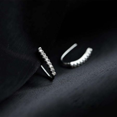 Primo piano degli orecchini a gancio in argento sterling che mostrano le brillanti pietre in zirconia cubica su uno sfondo di tessuto nero.