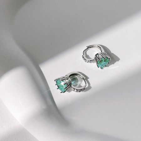 鮮やかな緑の宝石ときらめくアクセントが施されたエレガントなシルバーのイヤリングのペア。