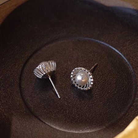 Un paio di orecchini in argento sterling esposti su una superficie scura, uno con la perla e uno che mostra la montatura a conchiglia vuota.