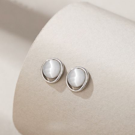 Un primo piano degli orecchini a perno in argento sterling con centri di pietra bianca minimalista su un supporto espositivo.