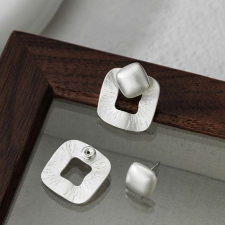Una collezione di orecchini dichiarativi in argento sterling, incluso il design quadrato, esposti su un telaio di legno.