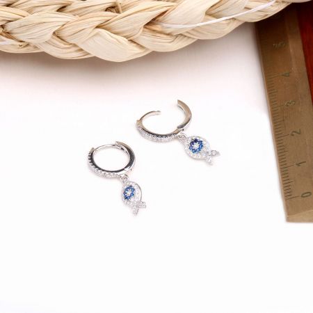 Un paio di orecchini a forma di pesce in argento dettagliati con gemme blu e bianche vivaci.