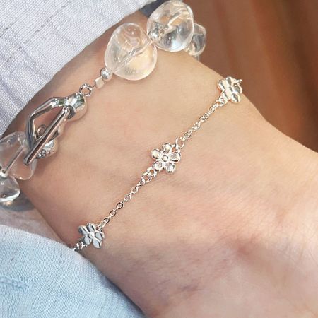Pulseras de cadena de charm de disco de flor de plata esterlina 925 al por mayor (conjunto de 5) - Un conjunto de pulseras de plata esterlina 925 al por mayor con charms de flores y cuentas transparentes, elegantemente usadas en una muñeca.