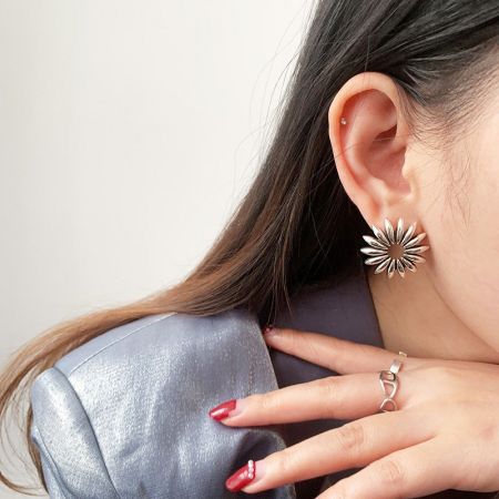 Scatto stilizzato di un orecchino a fiore in argento 925 insieme a anelli abbinati.