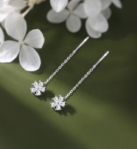 Lange Threader Bloemenoorbel in Sterling Zilver - Een paar lange threader bloemenoorbellen van 925 sterling zilver, met sprankelende cubic zirconia hangers, weergegeven op een groene achtergrond met witte bloemen.