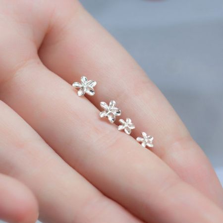 Een hand die drie verschillende maten van de zilveren bloemen stud oorbellen vasthoudt.