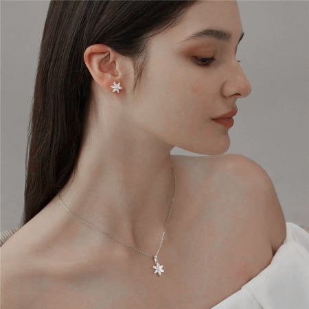 Un gros plan détaillé de la boucle d'oreille et du collier flocon de neige en argent, mettant en avant le savoir-faire.