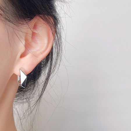 スリークな銀メッキの幾何学的フープイヤリングを着用したモデルが、そのフィット感とスタイルを披露しています。