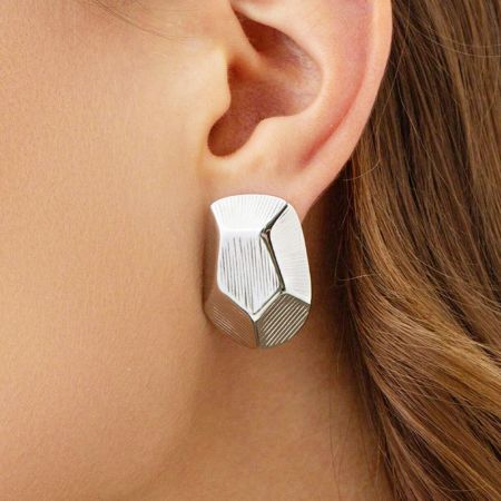 Een gedetailleerde close-up van de zilveren geometrische pentagon stud oorbel op een oor.