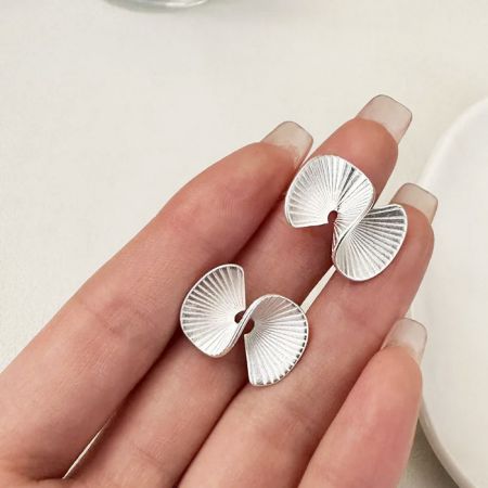Un primo piano degli orecchini a perno in argento ispirati alla foglia di ginkgo tenuti in mano.