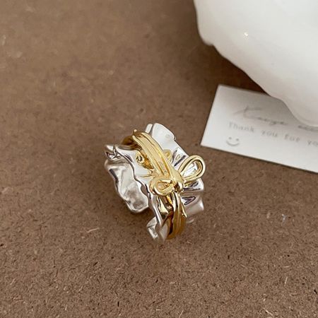Un anillo de lazo ajustable bicolor elegante en oro y plata, exhibido sobre un fondo neutro.