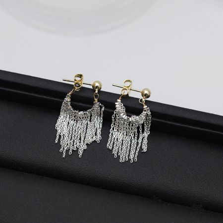 Un autre angle des boucles d'oreilles à franges en argent et or sur un fond blanc.