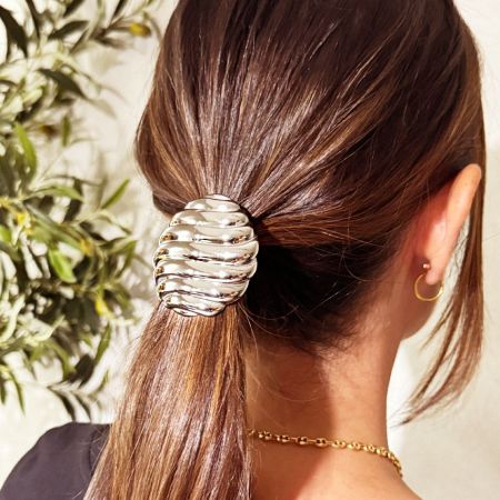 Un primer plano de una coleta de mujer asegurada con una cinta para el cabello de acero inoxidable con rayas plateadas.