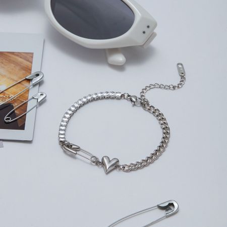 Närbild av hjärtcharm säkerhetsnåls tennisarmband i rostfritt stål med glittrande CZ-stenar.