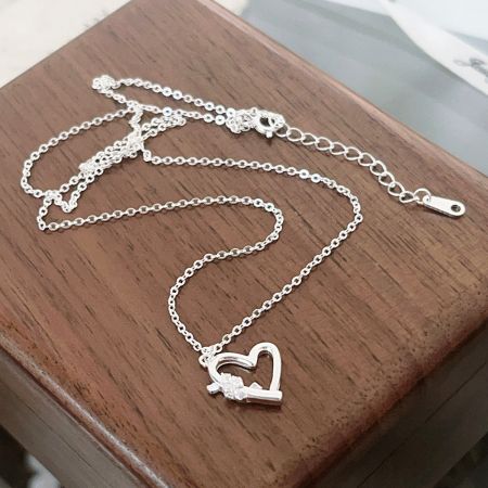 Gros plan sur un collier pendentif en argent sterling en forme de cœur et de flèche.