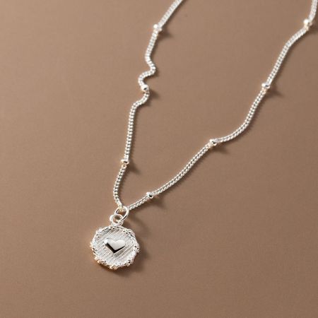 Collar de cadena con colgante de corazón de plata esterlina 925 - Un primer plano de un collar de plata esterlina 925 con un colgante de corazón pulido en una delicada cadena con cuentas, sobre un fondo blanco limpio.
