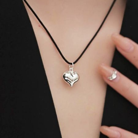 Vista detallada del colgante en forma de corazón de plata en su cordón negro.