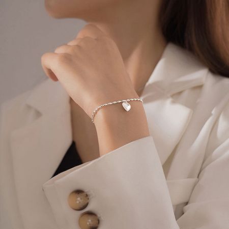 Conjunto de 5 pulseras de colgante en forma de corazón con cadena de cuentas de arroz de plata 925. - Un primer plano de la muñeca de una mujer que lleva una elegante pulsera de cadena con cuentas de arroz de plata esterlina 925 con un colgante de corazón pulido.
