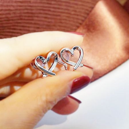 Dettaglio ravvicinato dell'orecchino a clip a forma di cuore in argento con un design interconnesso.