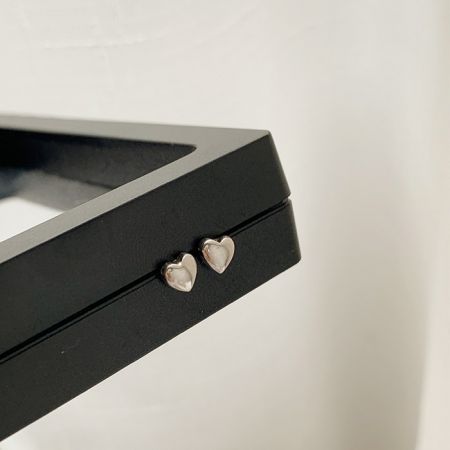 Los pendientes de corazón de plata elegantemente exhibidos en un marco negro para contraste.