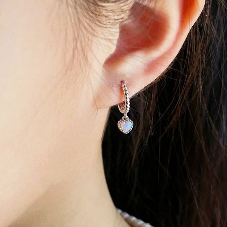 Modello che indossa l'orecchino huggie in opale a forma di cuore in argento sterling 925.