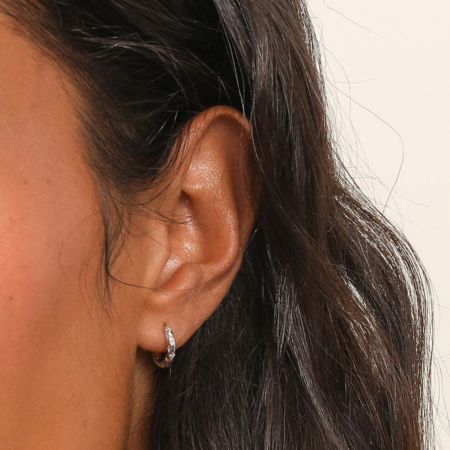 Primo piano di un orecchino huggie a cerchio con piercing a forma di stella in CZ argento indossato.