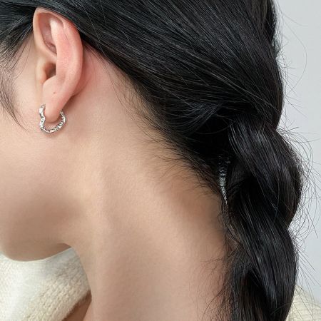 Modelo exibindo o ajuste elegante dos brincos de argola em forma de coração de prata minimalista.