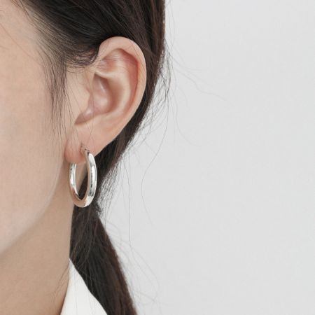 은 도금 마감 처리된 소형 두꺼운 후프 귀걸이를 착용한 여성의 클로즈업 뷰로, 우아한 핏을 강조합니다.