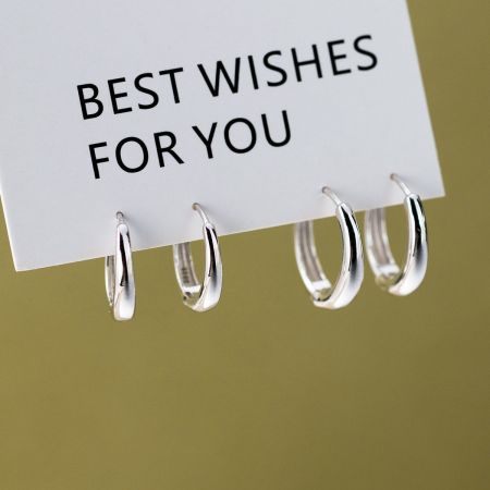 Un set di quattro orecchini a cerchio in argento esposti su un biglietto d'auguri con un messaggio sincero, perfetti per essere regalati.