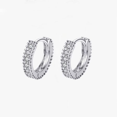 Un paio di orecchini huggie in argento sterling con pavé esposti su uno sfondo pulito.