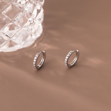 Vista ravvicinata di un paio di orecchini a cerchio huggie in argento con zirconia, evidenziando le pietre scintillanti.
