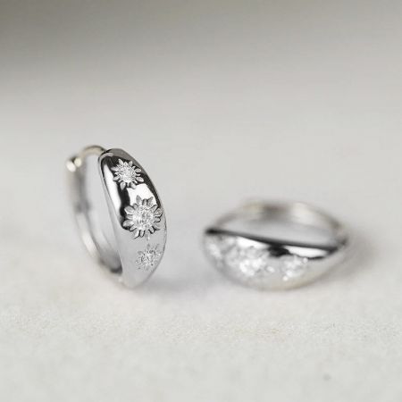 Primo piano degli orecchini huggie a cerchio in argento sterling con CZ a forma di stella, che mostrano il design floreale e di gemme intricati.
