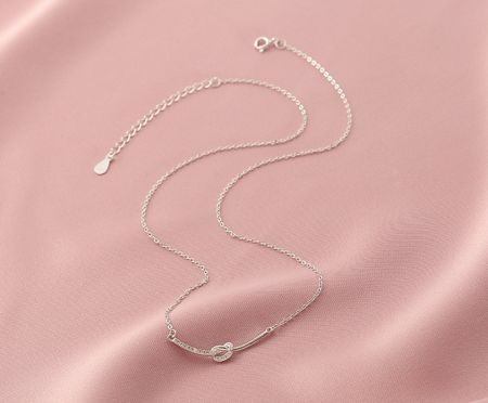 A stylish 925 sterling silver necklace with a unique knot design, displayed on a soft pink background.