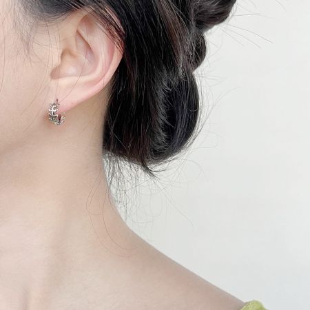 銀メッキの葉の花輪フープイヤリングを着用したクローズアップで、そのサイズとフィット感を示しています。